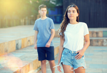 Young girl is standing and guy is walking behind her