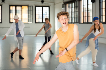 Fototapeta na wymiar Emotional teen boy practicing active dance movements with friends at group dance class