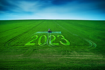 2023 Happy New Year concept and Aerial view of farming tractor plowing and spraying on field.