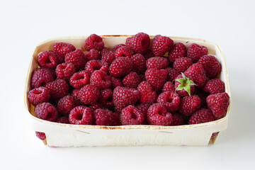 Raspberries in a rectangular wicker basket on a white surface, high angle, close-up. Ripe crimson berries in a filled basket, light background, copy space 