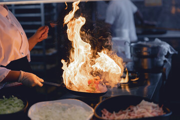 Concept professional chef and fire food. Woman cooking food vegetables open fire, photo slow motion freeze time. Concept hotel service pan asian wok