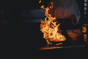 Process professional chef and fire pan. Woman cooking food vegetable open fire, dark background