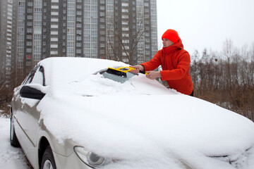 guy cleans the snow with a brush from the car, a man takes care of the car in winter