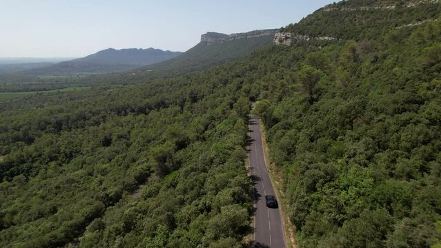 Electric car driving on a road passing through a forest south of France sunny aerial