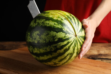 Woman cutting delicious watermelon at wooden table against black background, closeup