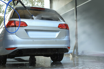 Washing auto with high pressure water jet at outdoor car wash, low angle view