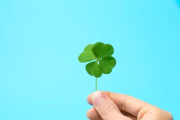 Fotobehang Woman holding beautiful green four leaf clover on light blue background, closeup © New Africa