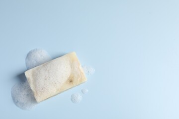 Soap with fluffy foam on light blue background, top view. Space for text