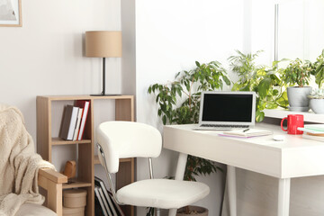 Stylish workplace with laptop on white desk near window