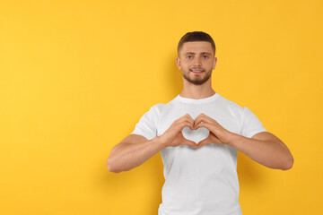Happy volunteer making heart with his hands on orange background. Space for text