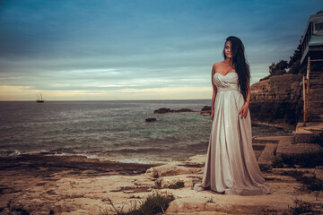 Fototapeta na wymiar Beautiful young woman in a white dress is enjoying the sun by the sea