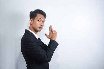 Playful and childish mature man with suit making gun gesture and blowing at the end of weapon as if he made a shot, expressing confidence and seriousness. Friend acts like spy on secret mission