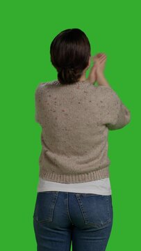 Vertical video: Back view of female person clapping hands and cheering people on camera, being cheerful and optimistic. Smiling woman applauding and saying congratulations, showing support standing