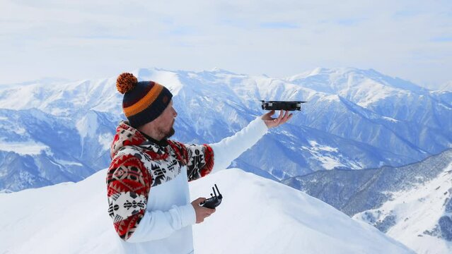 Happy man snowboarder in costume standing with remote control of flying drone or copter at snowy Swiss or Austrian mountains filming fantastic frames. Active lifestyle, extreme sport at Christmas time