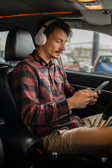 man with headphones listen music or podcast in car use mobile phone