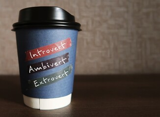 Paper coffee cup on copy space background with handwritten text - INTROVERT EXTROVERT AMBIVERT, Introverts tend to feel drained after socializing while extroverts tend to feel energized, ambivert is i