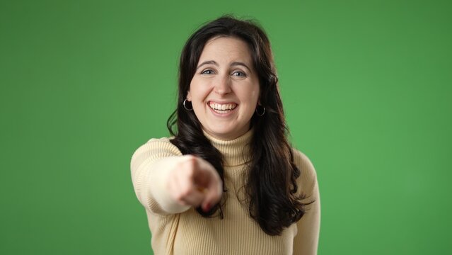 Young excited happy fun woman 20s look camera laugh smiling watch comedy movie pointing index finger on you isolated on green screen background studio portrait.