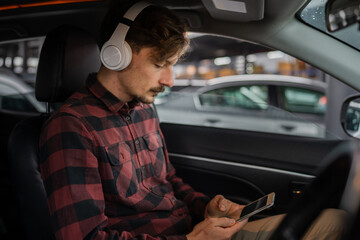 man with headphones listen music or podcast in car use mobile phone