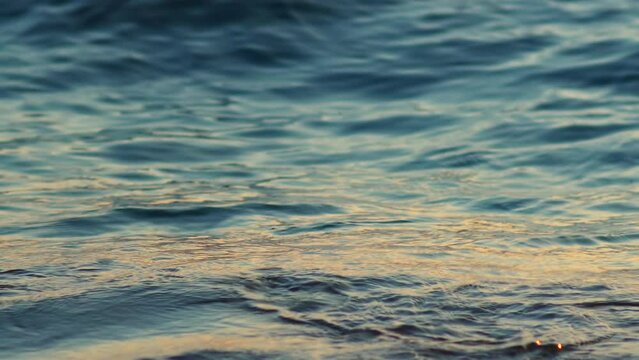 Sea, ocean surface with small waves and sunrise, sunset beams reflecting on the surface