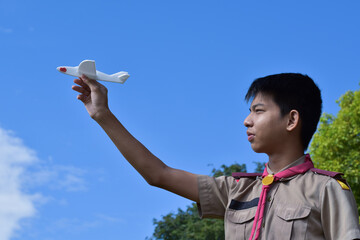 Asian boy scout holds white aroplane model against cloudy and bluesky background, soft and selective focus.