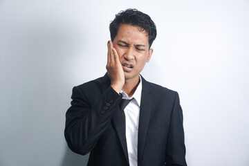 Tooth ache concept. Indoor shot of young male feeling pain, holding his cheek with hand, suffering from bad toothache, looking at camera with painful expression