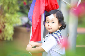 An Asian little girl who wearing a kindergarten uniform and has a wound sewn on her forehead playing alone outside
