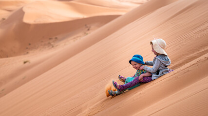 Two kids playing in the biggest sandbox in the world - in the Sahara desert. - obrazy, fototapety, plakaty