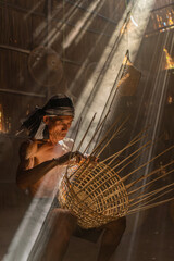 Moment a local northeast Thai male man adult uncle basket weaver maker hand making bamboo basket and hat in a dry grass built room