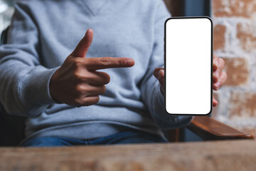Mockup image of a woman holding, showing and pointing finger at a mobile phone with blank white...