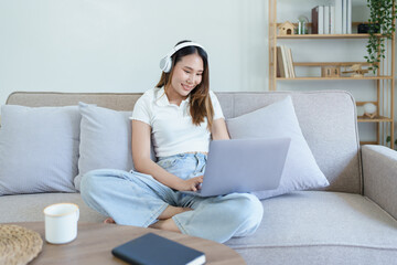 Obraz na płótnie Canvas asian teenage girl using computer and wearing headphones at sofa