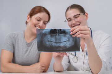 A woman doctor and a patient at the reception are discussing an x-ray of the jaw.