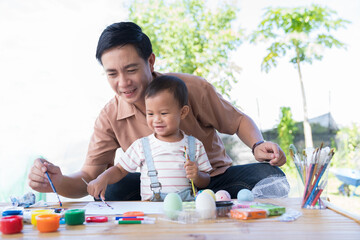 Father and baby little son painting eggs with brush in class workshop. Happy Asian dad embracing...