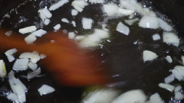 wooden spoon stirs onion and garlic in boiling sunflower oil, close-up