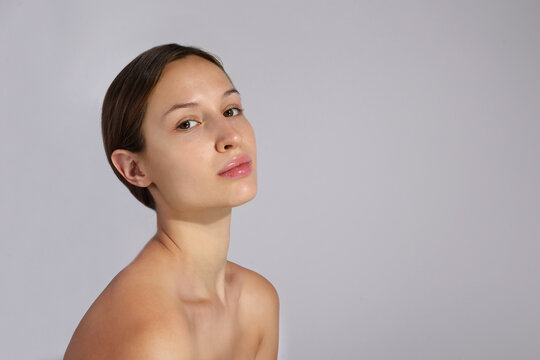 Studio portrait of young beautiful woman with long black hair tied in ponytail and clean face skin. Close up, copy space, isolated gray background.