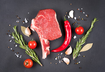 Raw beef steak with seasonings and vegetables over dark concrete table background. Cowboy steak...