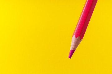 Colored pencil close-up with selective focus on the stylus and a blurred yellow background. Copy space