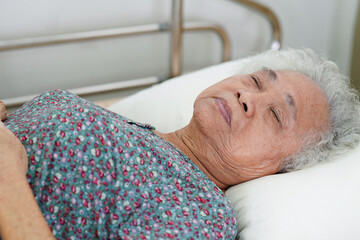 Asian elder senior woman patient holding bed rail while lie down with hope waiting her family in...
