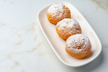 Homemade profiteroles with powdered sugar on white plate
