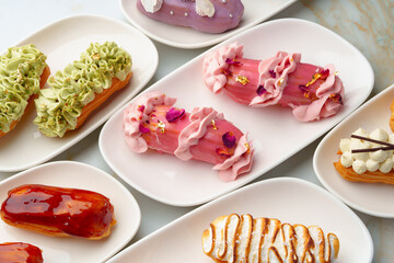 Set of colored eclairs with whipped cream on white plates