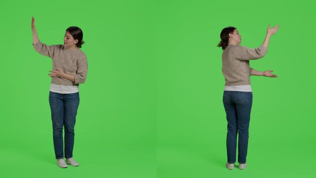 Friendly person doing advertisement and example sign in studio, standing over full body green screen backdrop. Casual relaxed woman showing presentation icon and advertising something.