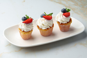 Cupcakes with strawberries and cream on white table