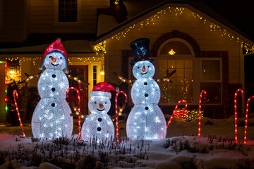 Glowing snowmen figures at night. Beautiful Christmas illuminated decorations outside the house....