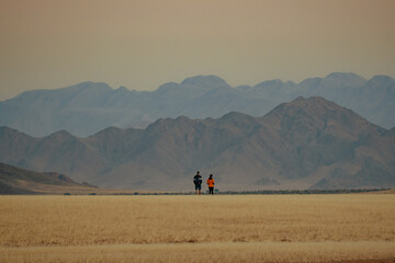 Zwei Touristen blicken im Abendrot in das Naukluft Gebirge in der Nähe von Sesriem (Namibia) - Powered by Adobe