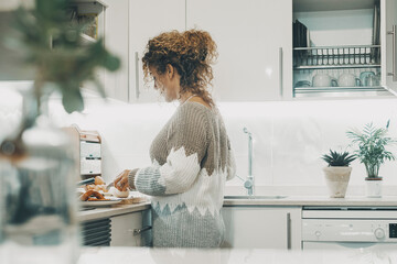 Side real view of woman cooking at home in the white minimal modern kitchen. One female people cook in indoor leisure pleasure activity alone. Wife or independent lady enjoying her time inside - Powered by Adobe