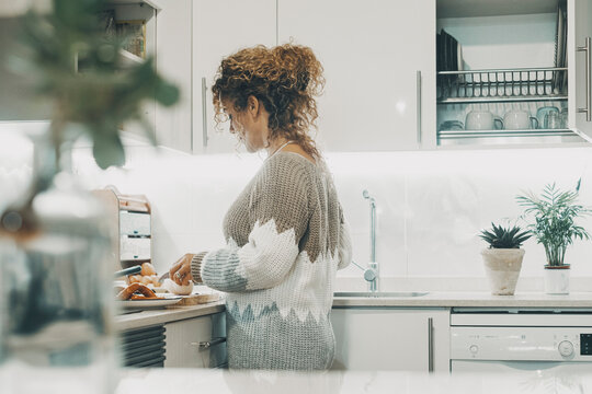 Side Real View Of Woman Cooking At Home In The White Minimal Modern Kitchen. One Female People Cook In Indoor Leisure Pleasure Activity Alone. Wife Or Independent Lady Enjoying Her Time Inside