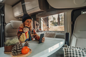 One woman living inside a modern camper van motorhome sitting at the table and using mobile phone to stay connected. Roaming connection technology for traveler female people in van life lifestyle