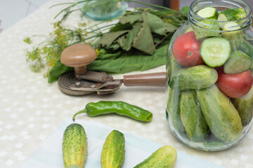 Cucumbers with green hot pepper on the table with glass jar with pickled vegetables cucumber and tomato with herbs and spices prepared for conservation. Selective focus. Harvest fall preparations 