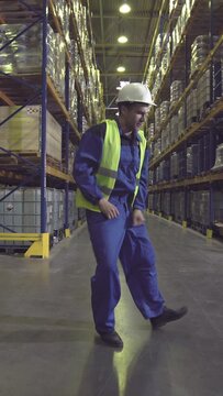 Warehouse worker dancing between racks in logistics center. Vertical video