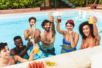 Millennial multiethnic friends celebrating at pool party raising fruit juice cocktails glasses and...