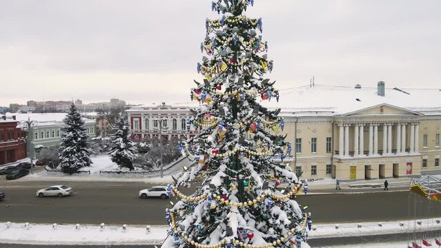 Christmas tree with golden beautiful garlands on the background of buildings. New Year's, green spruce fabulously decorated and covered with snow. City of Vladimir, Cathedral Square, Russia. UHD 4K.